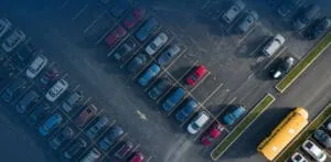 Aerial view of a commercial parking lot with marked spaces, parked cars, and a school bus