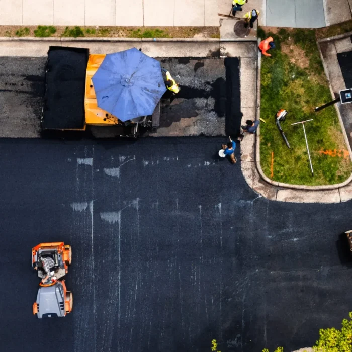 Commercial paving team applying new asphalt while compactors smooth the surface of a newly paved parking area.